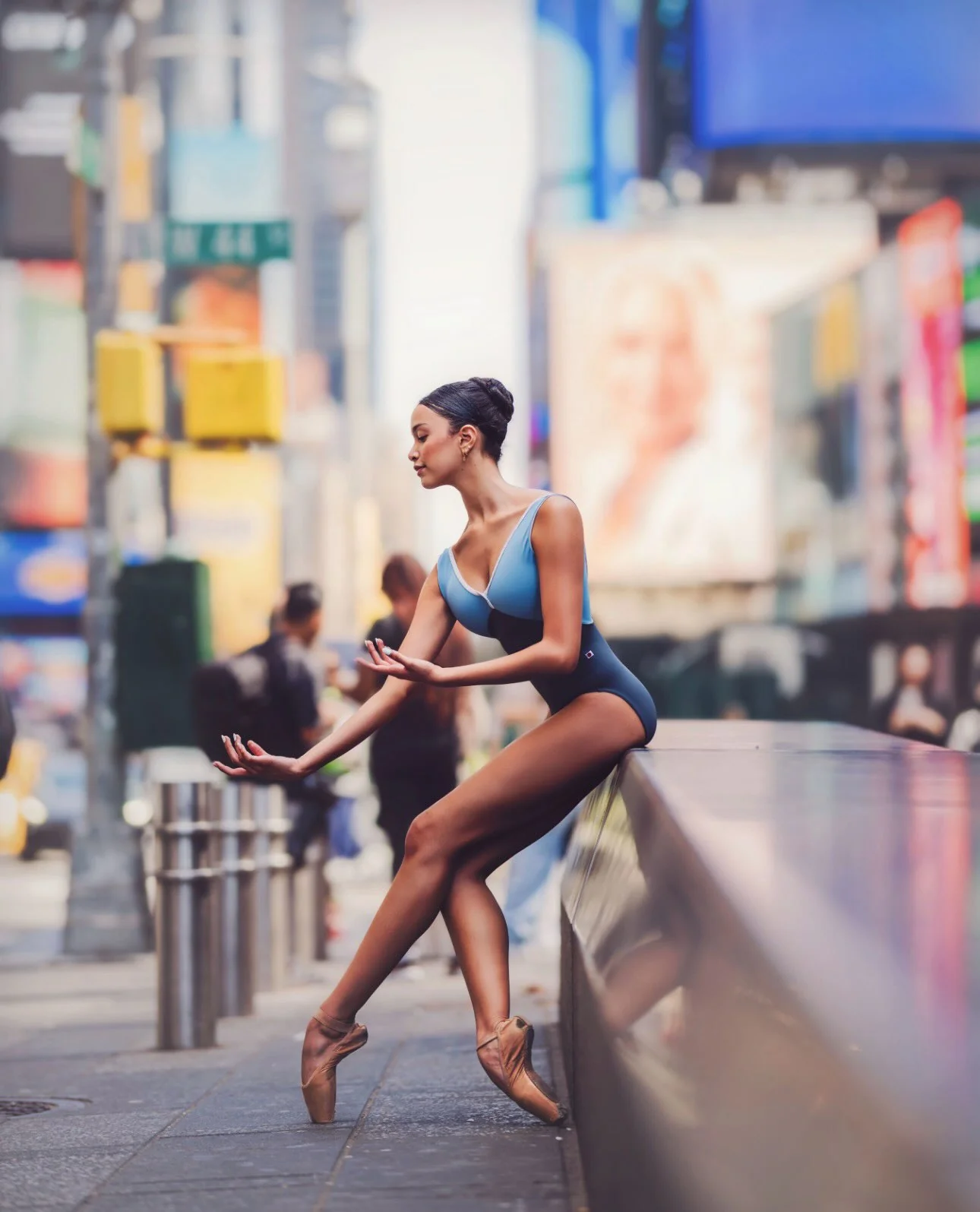 Grace in a blue leotard, seated en pointe in a reflective ballet pose in Times Square